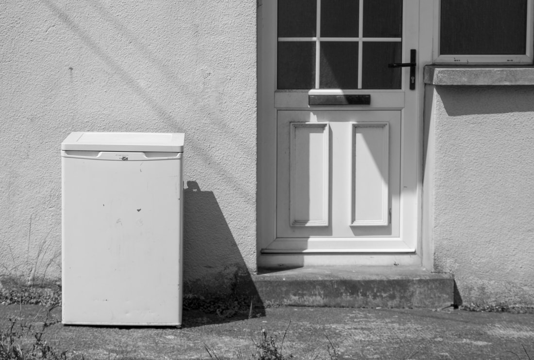 A white fridge outside of a house that has a white door 