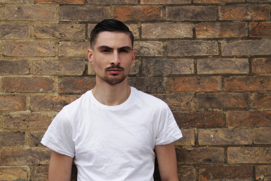 Male model in white shirt standing against on the brick wall besides to the street of London 