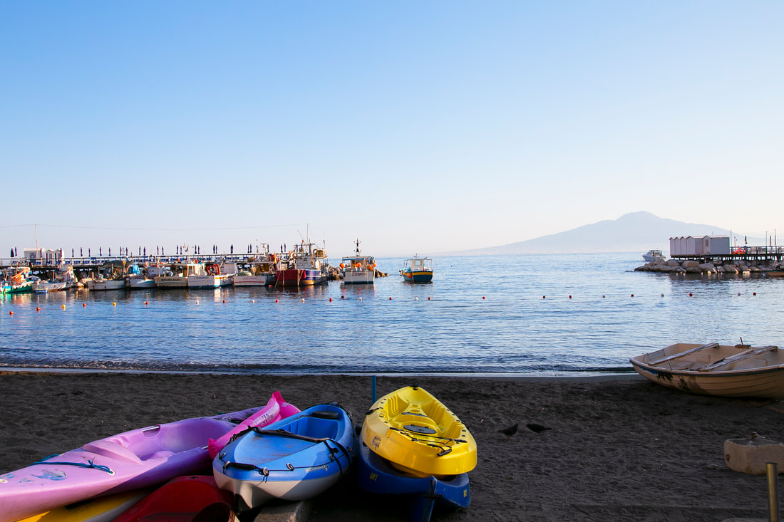 Pile of kayaks on the beach and boats on the sea with a mountain on the far end