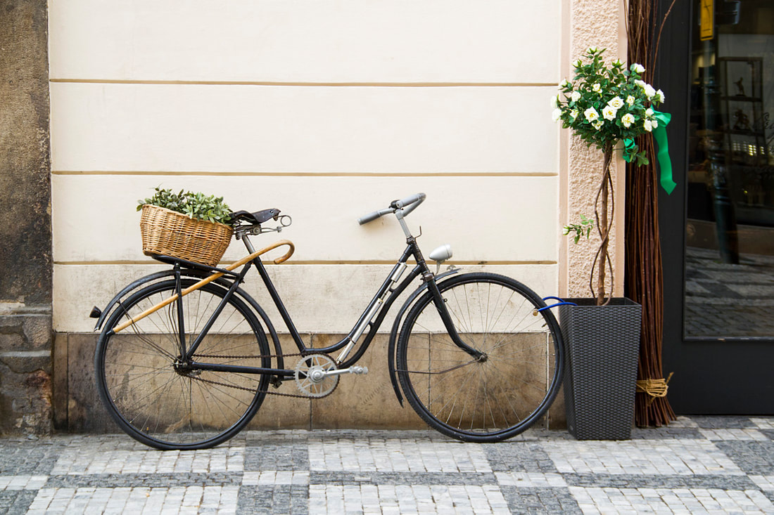 A bike leans on a wall with a basket of grass in the back and a walking stick on it.