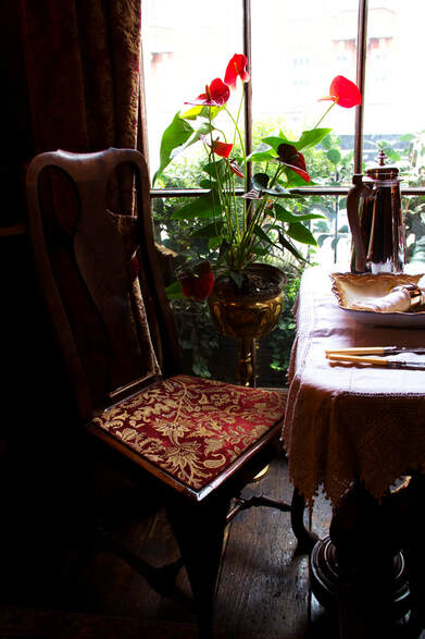 A chair with red and gold cushion, and table next to the window 