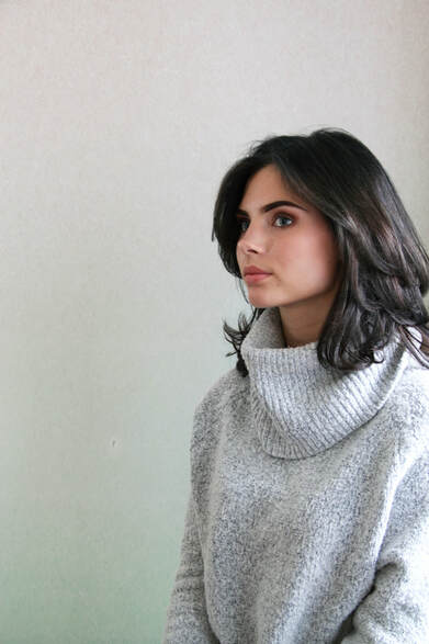 A female model in a grey jumper sitting next to window