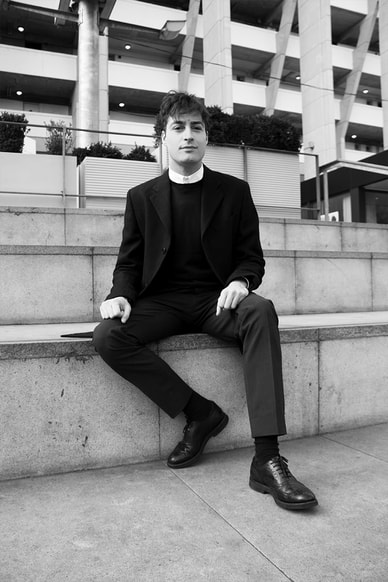 Male model with suit sitting on the stairs with buildings in the back 