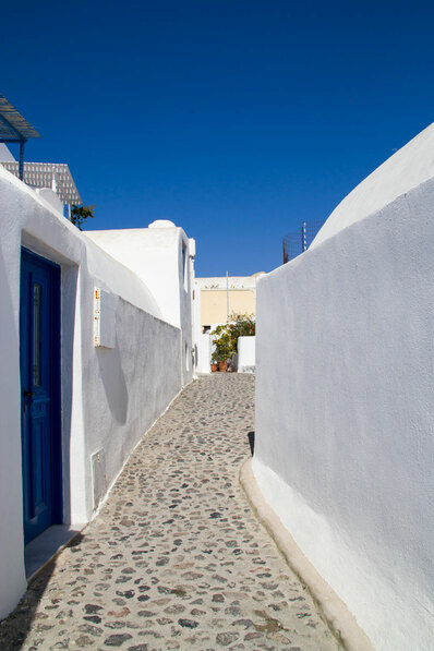 A alley way with white washed wall and blue doors beside it 