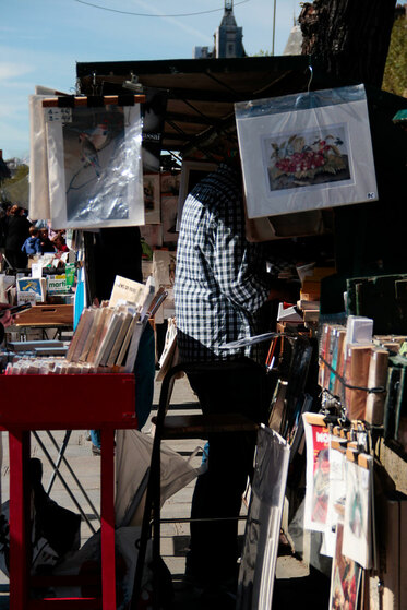  An old man browses paintings in the vendor besides the Seine in Paris.