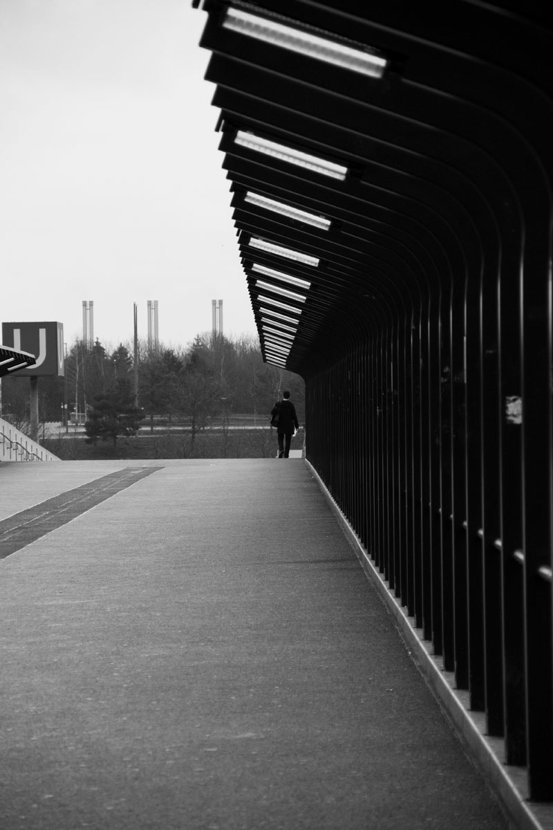 Black and white photography of a man walk on a bridge in Fröttmaning station, Munich.