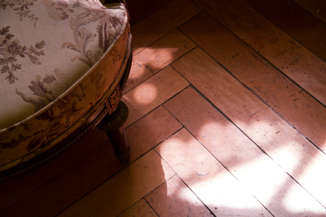 Old flower pattern chair with lights coming through windows and creates interesting patterns on the wooden floor.