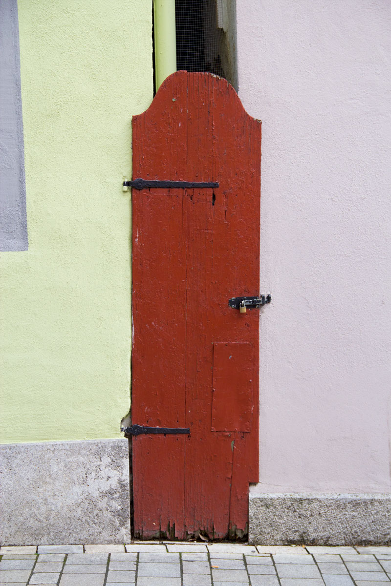 A dark red door sits in between light green and purple walls. 