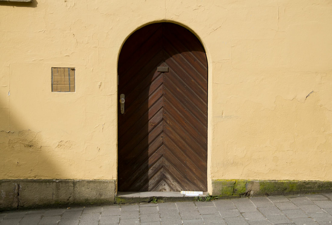 A yellow wall with a wooden arch door on the side of the road.