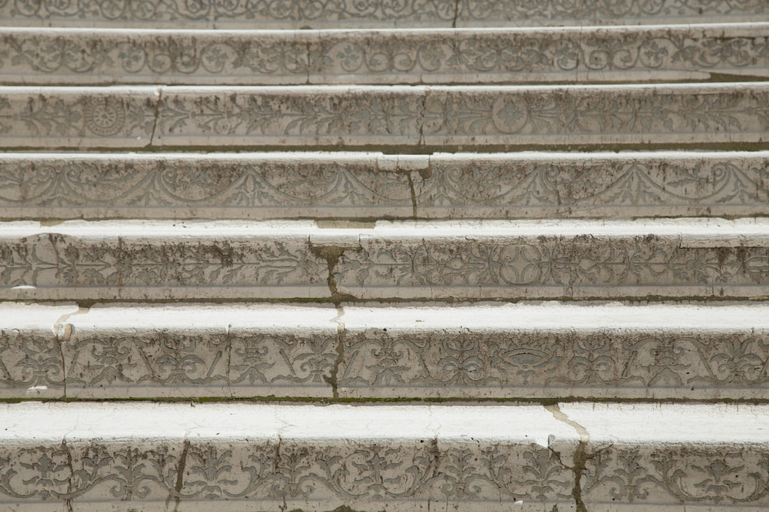 Gray and white stairs with plant carving design and cracks on them.