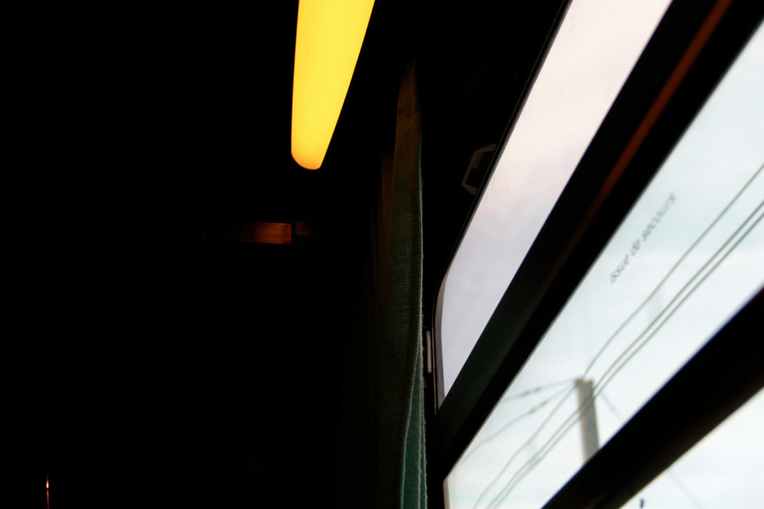 Yellow light sits on top of the train window next to the green curtain.