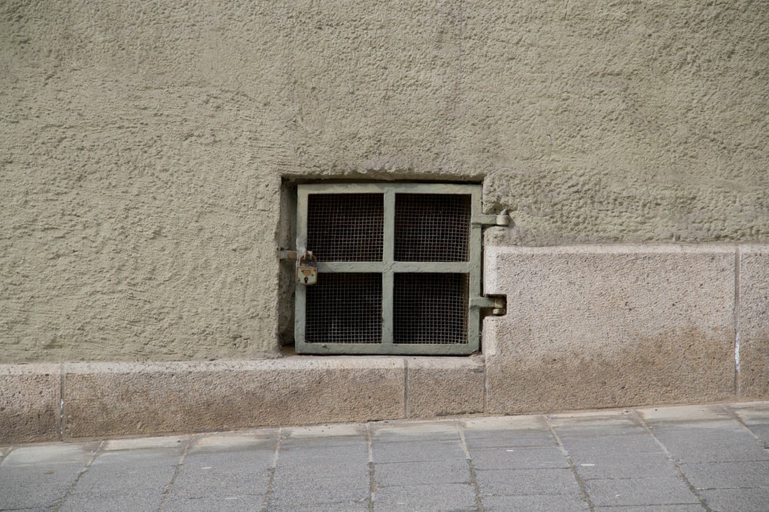 A hole on a green wall on the side of pavement with net window and green wooden frames. 