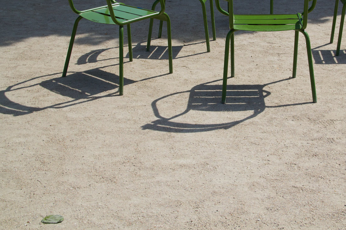 Green chairs create shadows under the sunshine in a park in Paris.