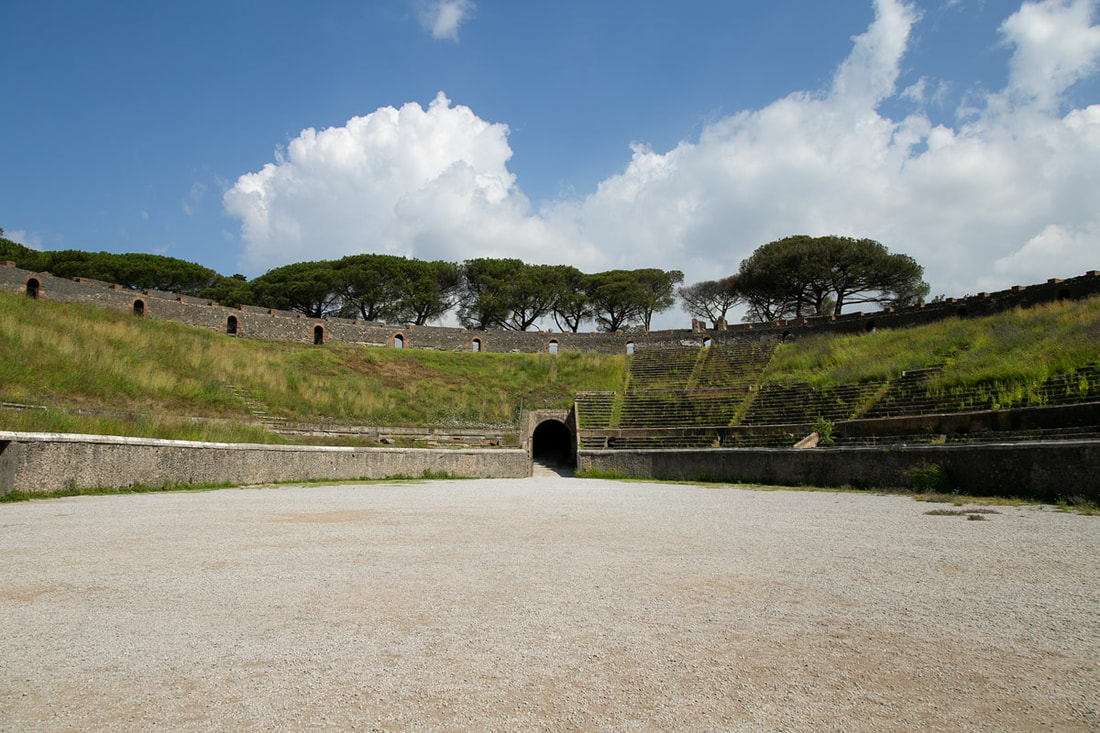 Sitting area full of grass in Amphitheatre of Pompeii with trees and blue sky in the back
