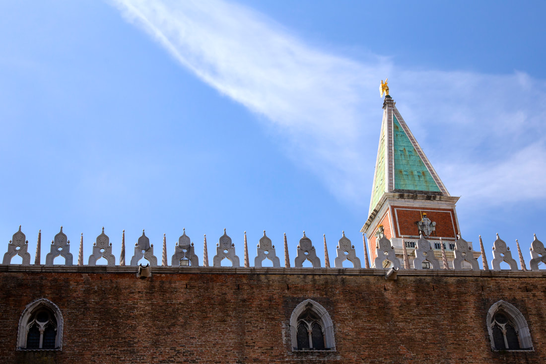 A red brick wall of Dog's palace in Venice and the top of St Mark's Campanile with blue sky.